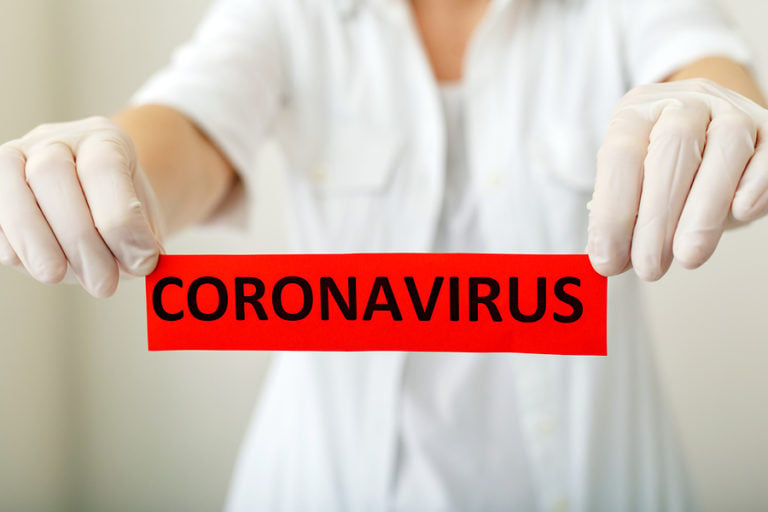 Nurse with gloves on holding up Coronavirus red sign