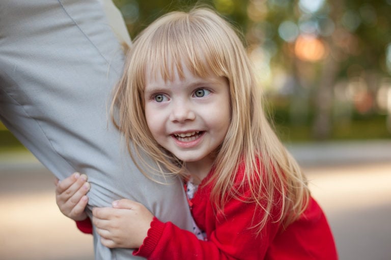 Little girl holding onto parents leg