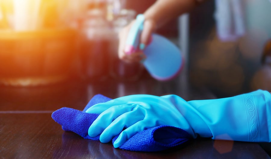 Spraying cleaning solution while wearing blue glove and using a cloth