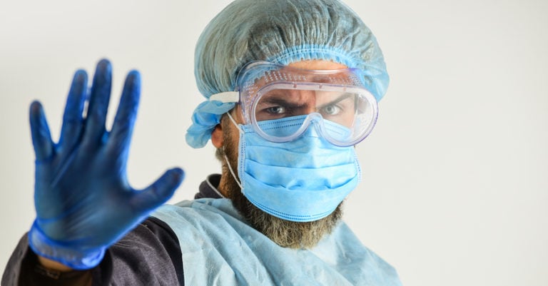 Male nurse wearing PPE gloves and mask with arm to say stop