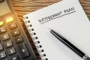 Pad of paper and pen with words "retirement plan" written on it next to calculator