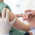 Nurse giving child a vaccination shot on right arm.