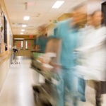 Blurred motion of doctor and nurse pulling stretcher in hospital hallway.