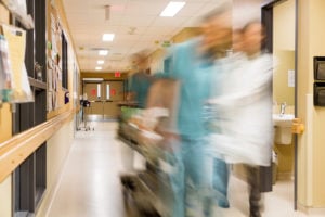 Blurred motion of doctor and nurse pulling stretcher in hospital hallway.