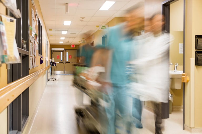 Blurred motion of doctor and nurse pulling stretcher in hospital hallway.