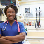 Black ER nurse smiling with arm crossed in ER room.