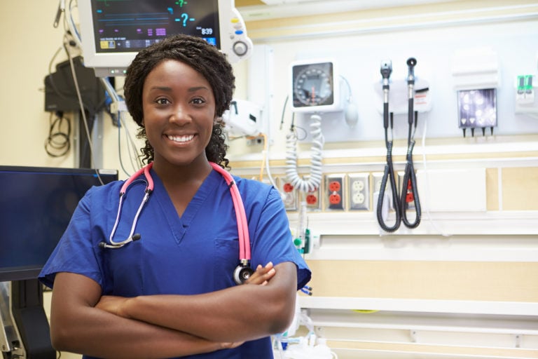 Black ER nurse smiling with arm crossed in ER room.