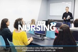 Nursing students sitting at tables with computers listen to a lecture.